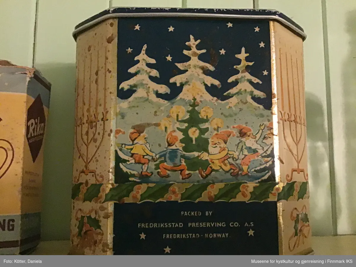 Boksen er åtte-kantet, har et lokk og er laget av blikk. Boksen er dekorert med ulike julemotiver, som nisser, juletrær, vinterlandskap, bjeller med sløyfer og femarmete lysestaker med stearinlys.