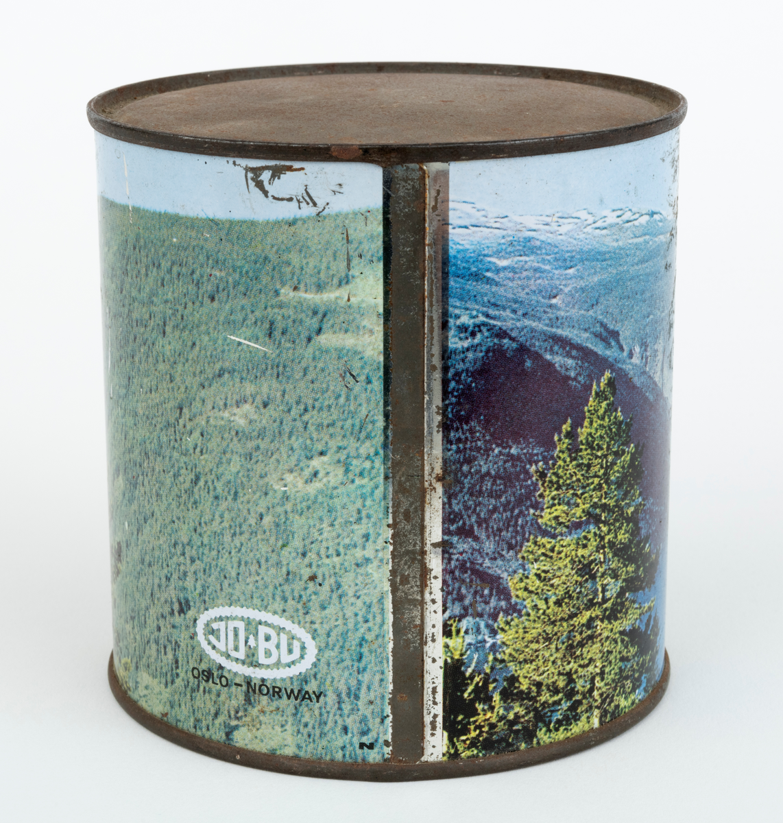 En sylindrisk boks, blikkboks, reklamemateriell, fra motorsagprodusenten / salgsbedriften Jo-Bu i Drøbak. Boksen har påtrykt firmaets logo og et bilde av motorsaga Jo-Bu (JOBU) L7. Saga svever over et norsk fjordlandskap med skogkledte fjellsider i forgrunnen og snødekte fjelltopper i bakgrunnen. Logoen som er påtrykt blikkboksen består av navnet JO BU med et grantre mellom JO og BU. Navnet omkranses av et sagkjede. Under "sagkjedet" står teksten: "OSLO-Norway".

Boksen har ukjent innhold, men en hører en raslelyd når den ristes.