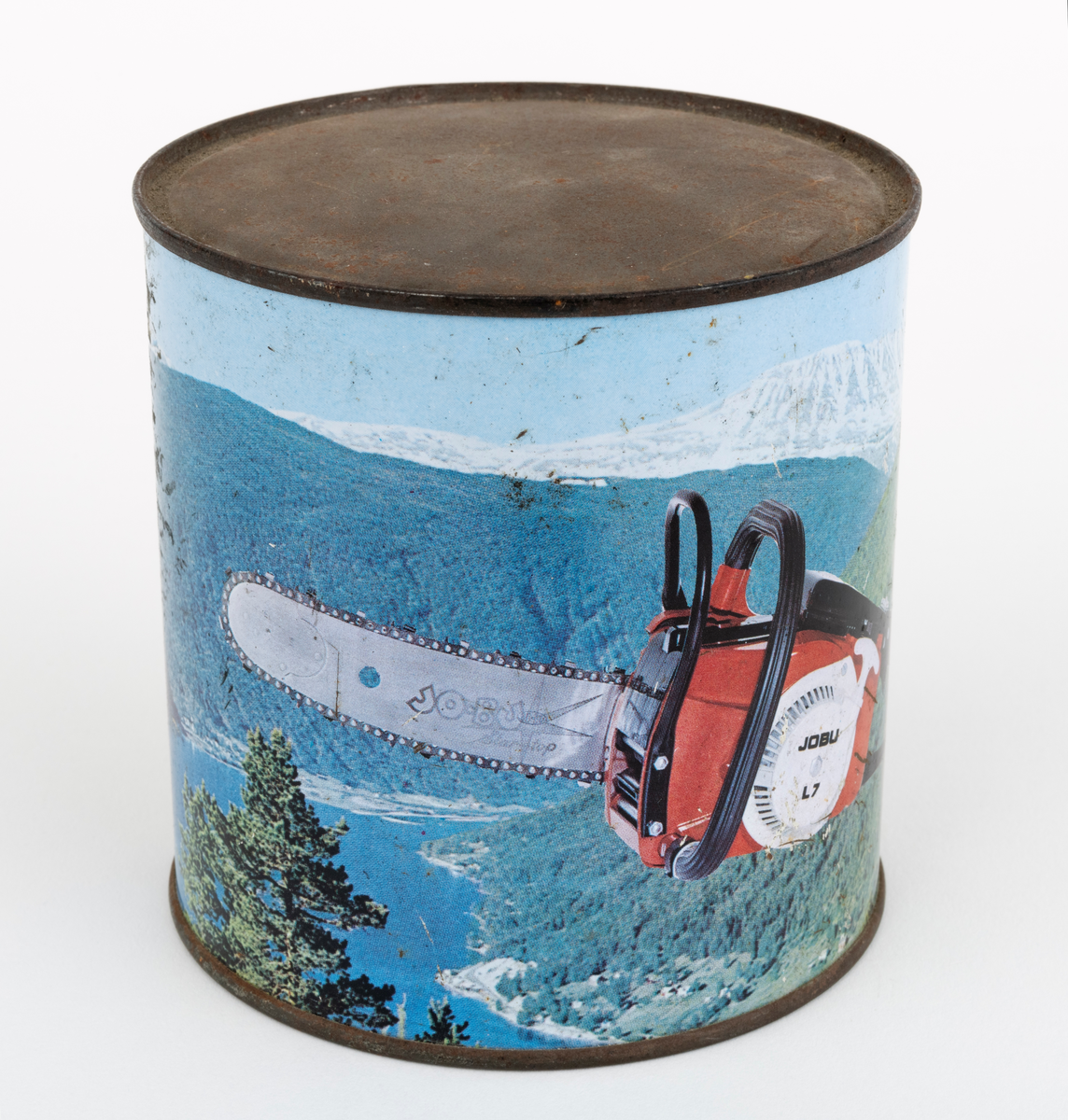 En sylindrisk boks, blikkboks, reklamemateriell, fra motorsagprodusenten / salgsbedriften Jo-Bu i Drøbak. Boksen har påtrykt firmaets logo og et bilde av motorsaga Jo-Bu (JOBU) L7. Saga svever over et norsk fjordlandskap med skogkledte fjellsider i forgrunnen og snødekte fjelltopper i bakgrunnen. Logoen som er påtrykt blikkboksen består av navnet JO BU med et grantre mellom JO og BU. Navnet omkranses av et sagkjede. Under "sagkjedet" står teksten: "OSLO-Norway".

Boksen har ukjent innhold, men en hører en raslelyd når den ristes.