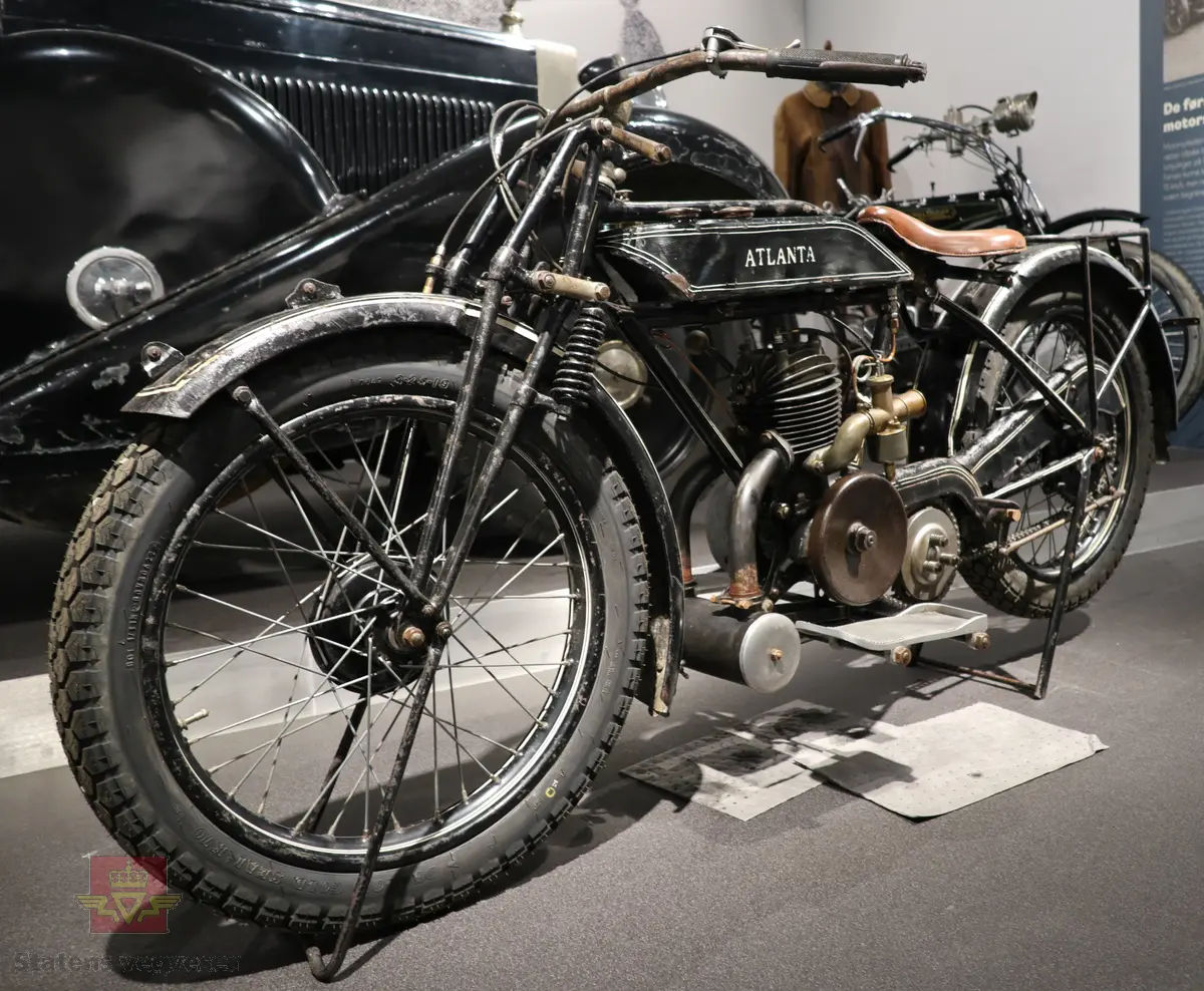 Atlanta. Motorsykkel, svart med hvit staffering. Motoren er en ensylindret bensindrevet forbrenningsmotor fra Villiers med et sylindervolum på 342 ccm (350) og en effekt på 8-12 hk. Albion 3-gir med clutch og kick starter. Sykkelen mangler noen deler. Atlanta med Villiers motor benevnes gjerne som Atlanta-Villiers. Merkingen CZ på veivhuset og Mark IXB på sylinder beviser at dette er en Villiers på 342 ccm fra perioden 1926-1929 (trolig org. motoren).