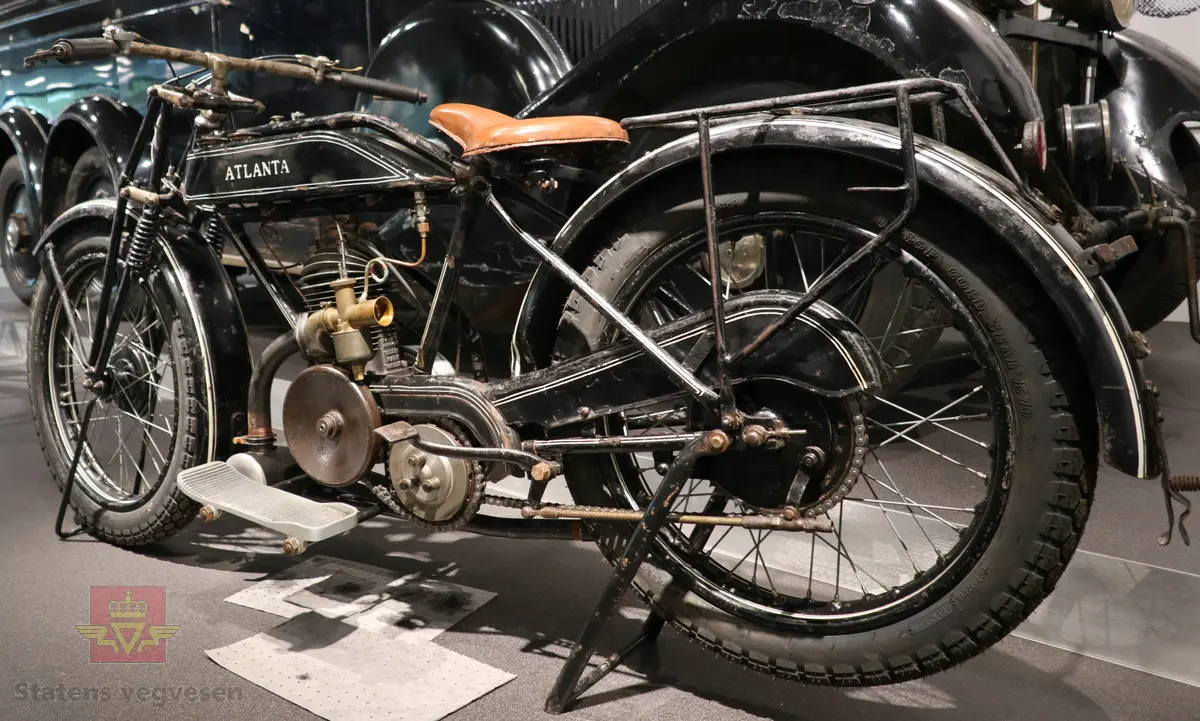Atlanta. Motorsykkel, svart med hvit staffering. Motoren er en ensylindret bensindrevet forbrenningsmotor fra Villiers med et sylindervolum på 342 ccm (350) og en effekt på 8-12 hk. Albion 3-gir med clutch og kick starter. Sykkelen mangler noen deler. Atlanta med Villiers motor benevnes gjerne som Atlanta-Villiers. Merkingen CZ på veivhuset og Mark IXB på sylinder beviser at dette er en Villiers på 342 ccm fra perioden 1926-1929 (trolig org. motoren).
