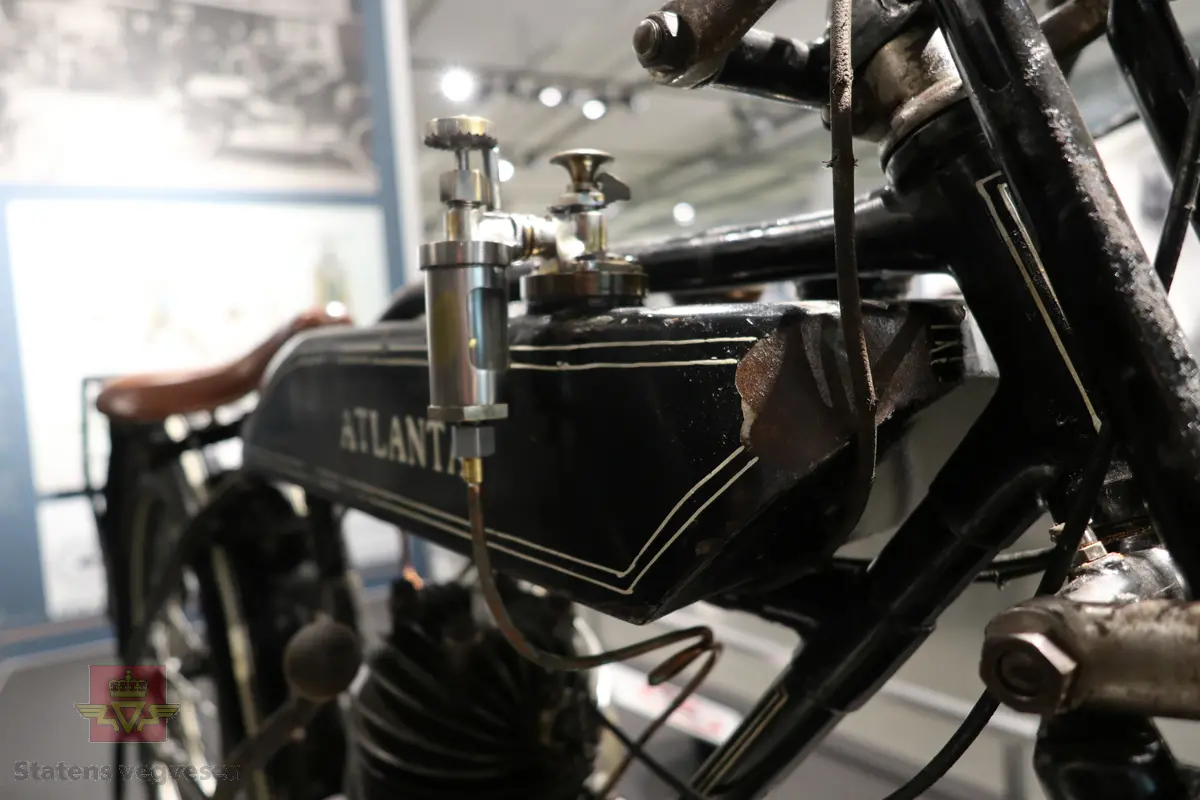 Atlanta. Motorsykkel, svart med hvit staffering. Motoren er en ensylindret bensindrevet forbrenningsmotor fra Villiers med et sylindervolum på 342 ccm (350) og en effekt på 8-12 hk. Albion 3-gir med clutch og kick starter. Sykkelen mangler noen deler. Atlanta med Villiers motor benevnes gjerne som Atlanta-Villiers. Merkingen CZ på veivhuset og Mark IXB på sylinder beviser at dette er en Villiers på 342 ccm fra perioden 1926-1929 (trolig org. motoren).
