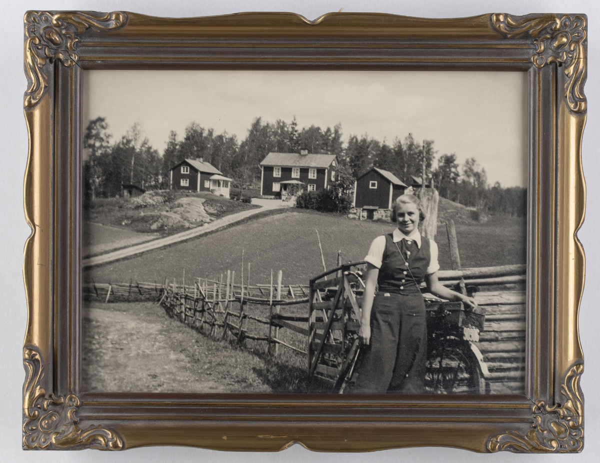 Svartvitt fotografi i ram.

Fotografi av en kvinna som står lätt lutad mot en cykel i en lantlig miljö. I bakgrunden finns en gärdesgård, väg och tre byggnader. 
Kvinnan är klädd i vida byxor, knäppt väst och kortärmad blus med krage. Kvinnan heter Ulla Zander och det är gården Holmbo i Hannäs i bakgrunden.

Fotografiet sitter i en brun- och guldfärgad ram, tillvekad av trä och ornerad med gips. Ramen har ett bakstycke av brunmarmorerad papp med ett ståstöd. Framför fotografiet sitter ett glas. Fotografiet, glaset och bakstycket skjuts in i ramens ena kortsida. Ramen är ihopspikad med nubb i hörnen.

Fotografiet finns i arbetarhemmet Solliden, som flyttades till Gamla Linköping 1987. I Solliden bodde Nils Andersson med sina föräldrar, Albin, som var diversearbetare, och Elisabeth, som var hemsömmerska. Hemmet har bevarats nästan helt orört sedan andra hälften av 1920-talet, då familjen Andersson flyttade in i  det nybyggda huset, som tidigare låg på Sandtorpsgatan i Linköping.

Ulla, på fotografiet, var kusin till Nils och hon bodde under perioder i barndomen i Solliden. Gården Holmbo var Elisabeths och Ullas pappa Enochs föräldrahem.