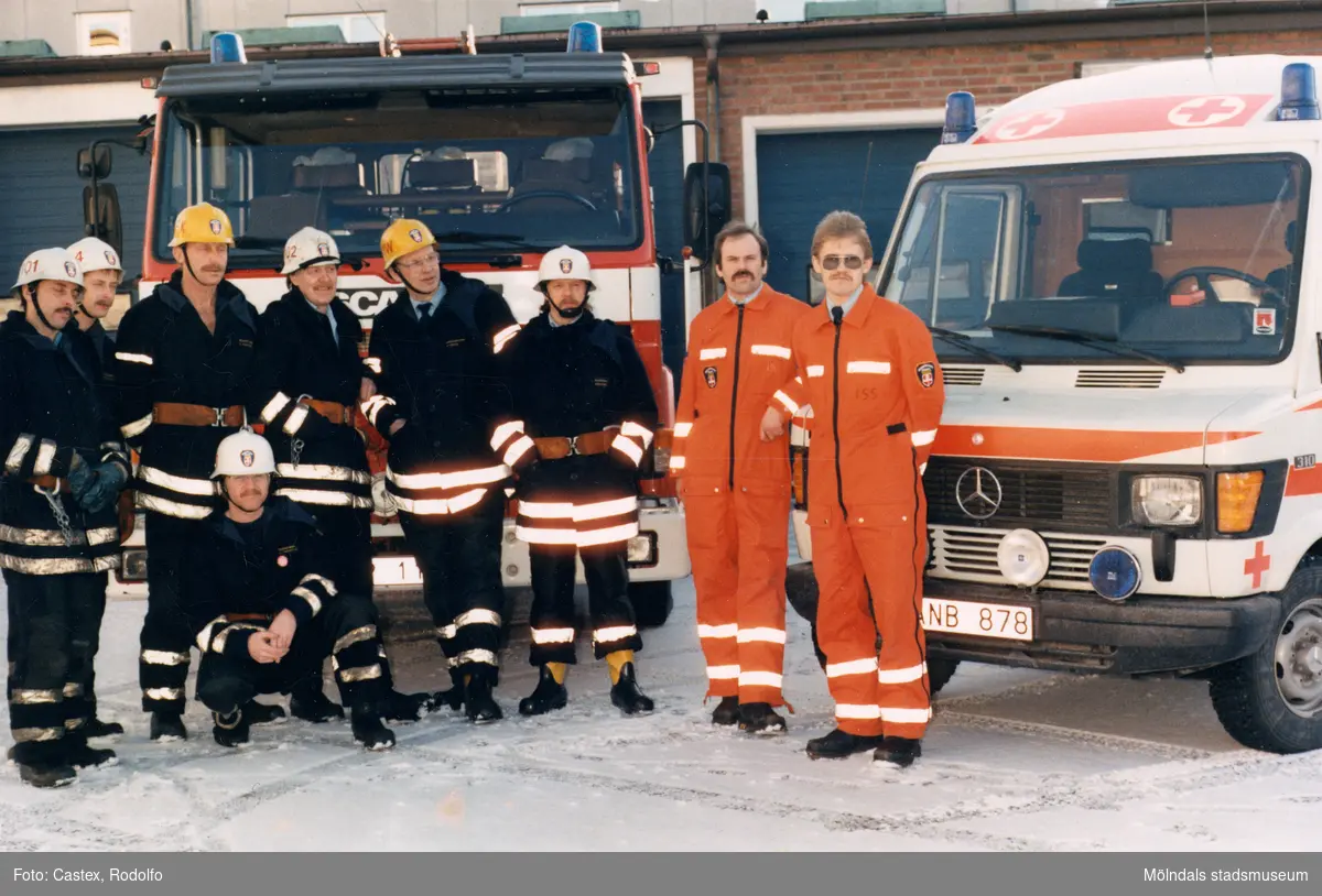 Mölndals brandstation i Trädgården, Mölndal, på 1980-talet. En samling brandmän och ambulansförare står uppställda vid sina fordon.