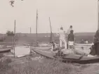 Kanoter och kanotister vid Fjäderholmarna. I förgrunden kajak uppdragen på land. I bakgrunden segelkanoter och roddbåt.