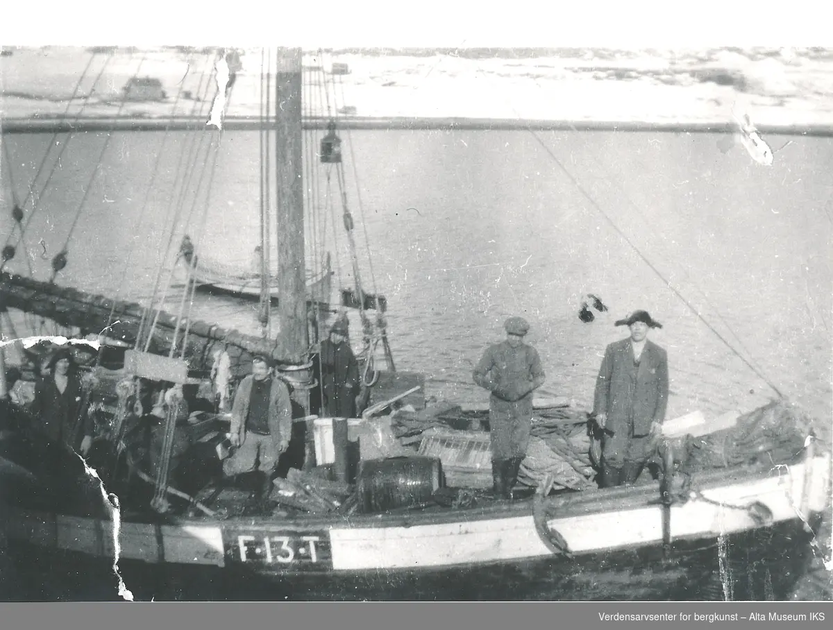 Flere mennesker står i en seilbåt, F13T,  som ligger til kai i Talvik. Bak båten ligger det andre mindre båter på fjorden.