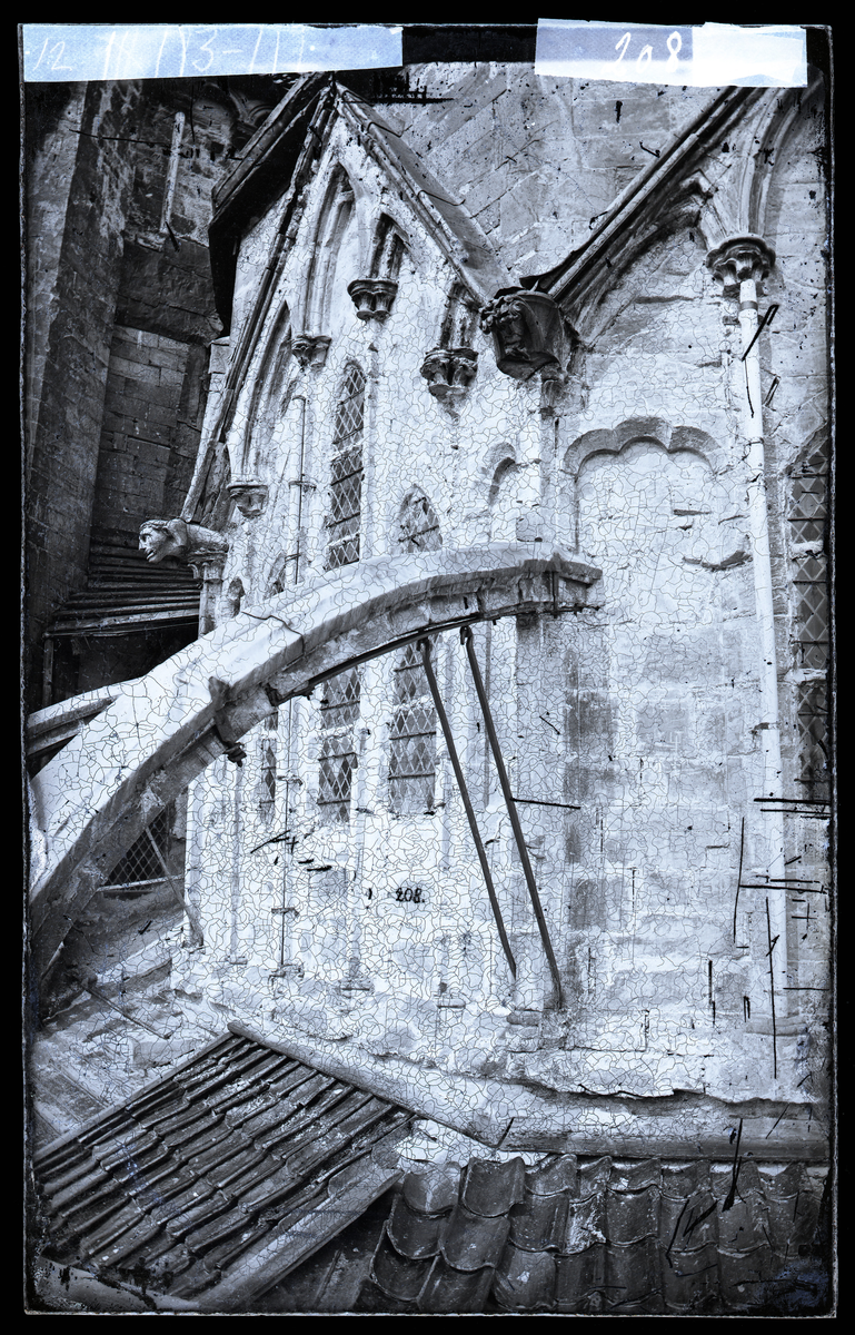 Søndre veggparti i klerestoriehøyde i oktogonen i Nidarosdomen. Strebebuer og gotisk skulptur med ansikt. Gamle blyglassvindu. Bildet er tatt før restaurering av oktogonen, et arbeid som pågikk i perioden 1872-1877.