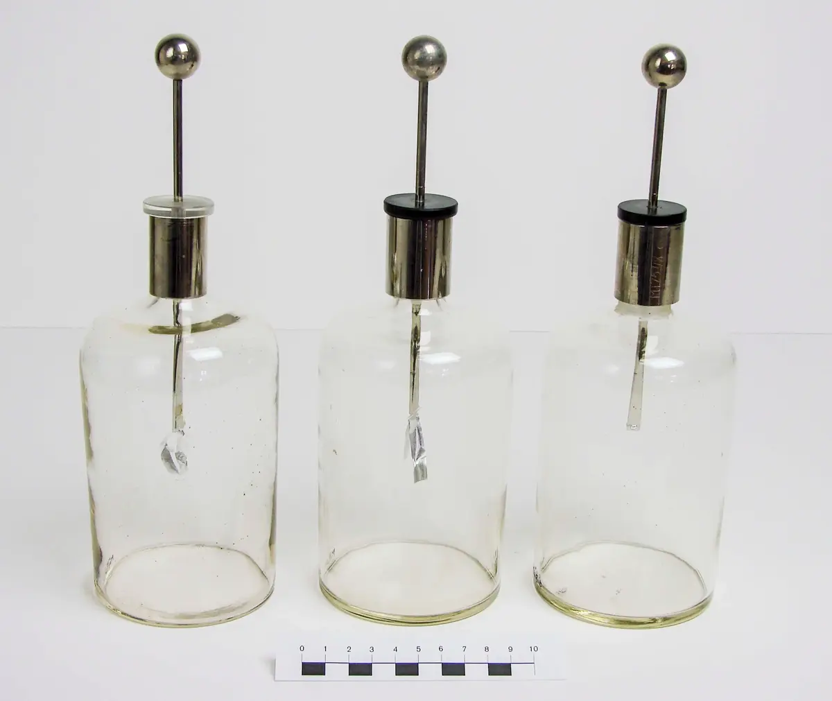 A) Bladelektroskop, glasflaska, höjd 18 cm, diam. 8,3 cm. Halsen har cylindrisk hylsa, av aluminium, höjd 3,5 cm. Propp av glas, genomborrad av en rundstav, i nedre änden tillplattad, med 2 st. tunna aluminiumblad, längd 3,5 cm, fästa i yttersta delen. Staven kröns av en kula, av aluminium, diam. 1,9 cm. Ena aluminiumbladet trasigt.

B) Bladelektroskop, glasflaska, höjd 17,5 cm, diam. 8,5 cm. Hals med cylindrisk hylsa, av aluminium, propp av hårdgummi, svart, genomborrad av rundstav, nedre änden tillplattad, med 2 st. aluminiumblad, krönt av kula, av aluminium, diam. 1,9 cm. 

C) Bladelektroskop, glasflaska, höjd 17,5 cm, diam. 8,5 cm. Hals med cylindrisk hylsa, av aluminium. Propp av hårdgummi, svart, genomborrad av aluminiumstav, tillplattad nedre ände, med 2 st. aluminiumblad, det ena trasigt. Krönt med kula, av aluminium, diam. 1,9 cm. 


Till kulan förs en laddad stav, strömmen leds genom rundstaven ner i bladen, vilka repellerar eftersom de laddats med samma slags elektricitet. 