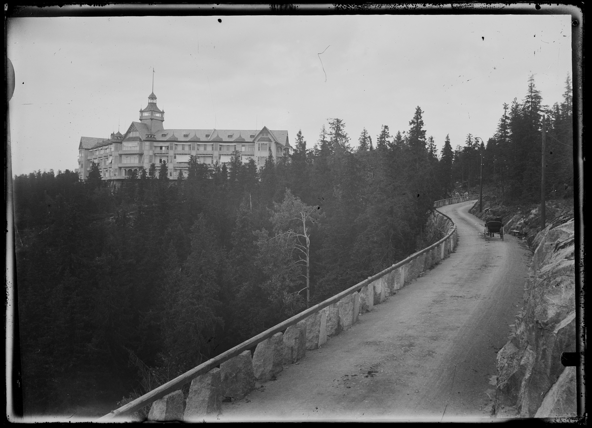 En vei går gjennom en barskog, med stabbesteiner langs venstre side. På en høyde i skoglandskapet ligger Voksenkollen Sanatorium, med tilnavnet «Soria Moria», som åpnet i 1900 og brant ned i 1919. 