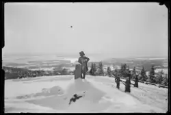 En statue av en mann med hatt og frakk er plassert på en høy