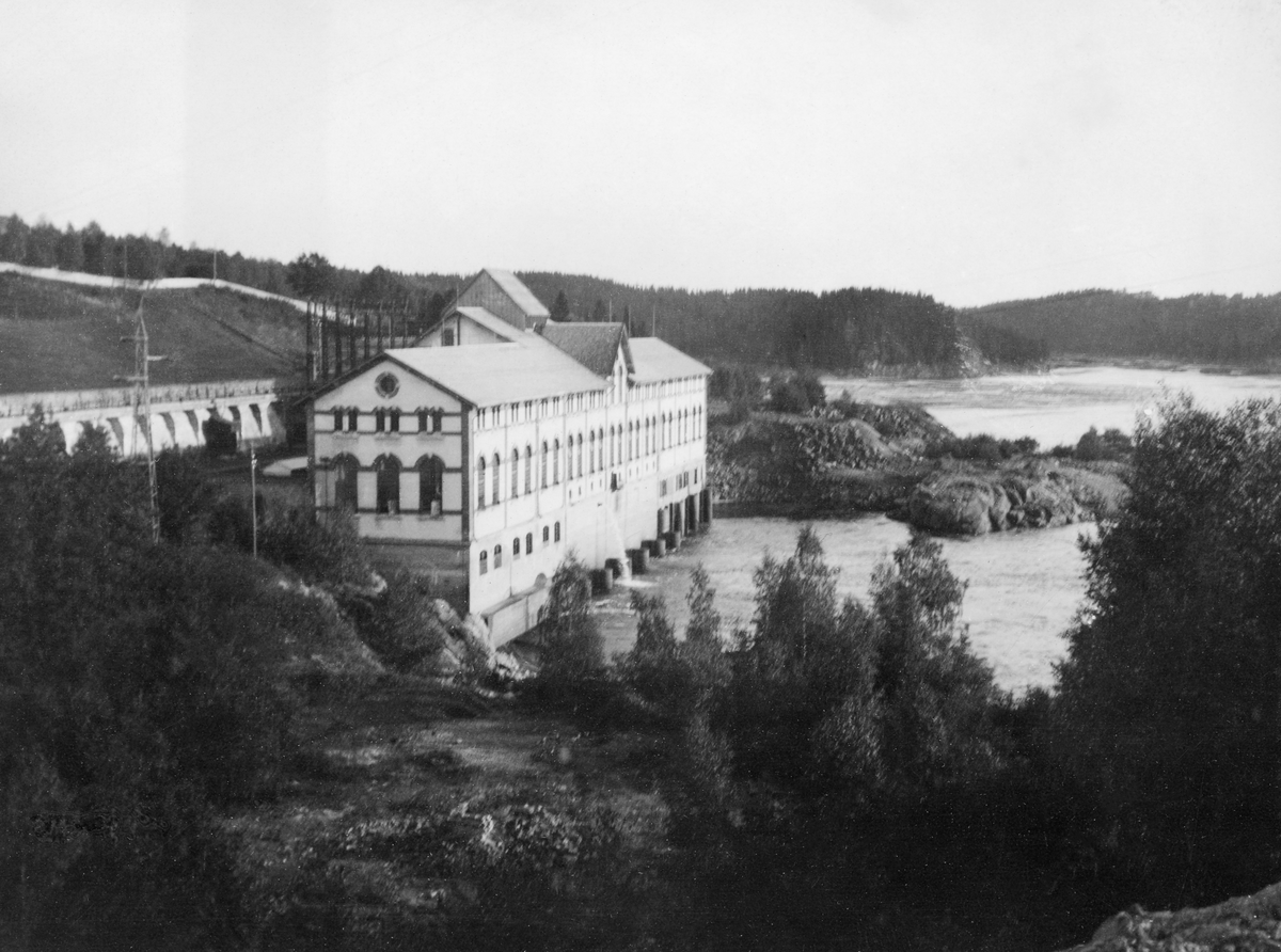 Oversiktsbilde mot kraftverket ved Kykkelsrud i Askim og den foranliggende Rudshverven, ei bakevje i Glomma, der fløtingstømmeret hadde lett for å bli gående i en roterende strøm.  Fotografiet er tatt fra en bakkekam eller bergknaus sør for anlegget. 