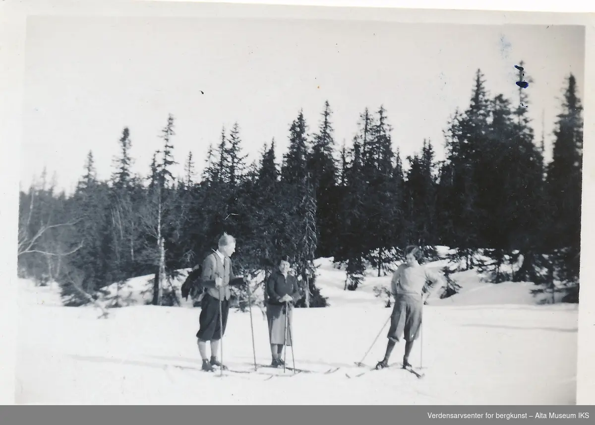 En mann og to kvinner går på ski over en slette, bak dem er en skog.