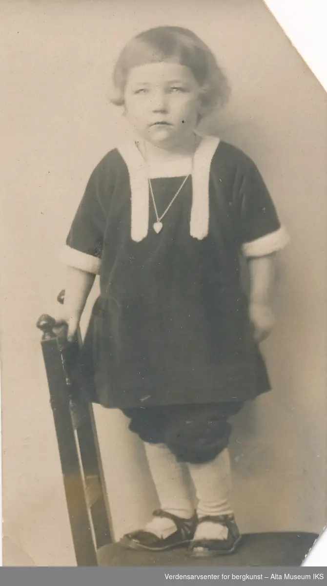 Portrett av et barn som står på en stol og ser på kameraet. 