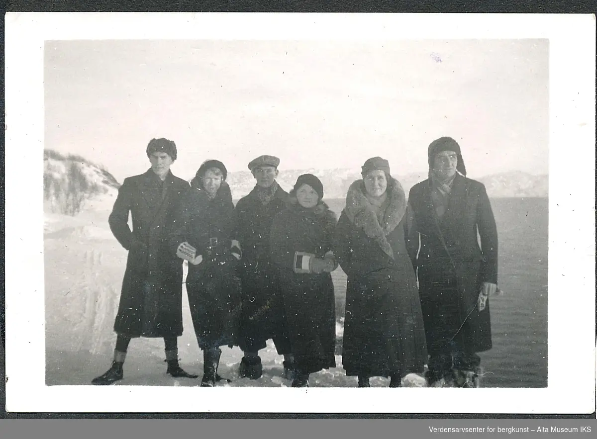 Tre menn og tre kvinner i vinterklær står ved sjøen.