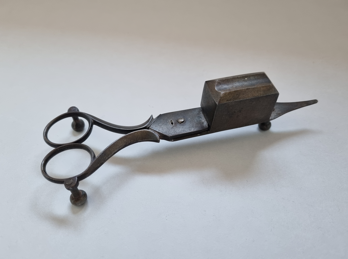 Ljussax i brons. Ljussaxen användes innan den självförintande veken uppfanns. Behållaren är avsedd för den avklippta veken. Spetsen är till för att räta upp veken med. Saxen vilar på tre fötter för att inte sota ner underlaget.