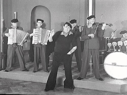 Bert Renées orkester med ordinarie trumslagare främst i utstyrsel som nog ska föreställa en sjöman från sydligare nejder i byxor breda nedtill, "basker", tjusarlock i pannan, scarf och armtatueringar. På bild 2 (med högre upplösning) framgår att det ena dragspelet är av märket Settimio Soprani, vilket är ett av Italiens äldsta varumärken. År 1863 startade Paolo Soprani företaget Soprani tillsammans med sina bröder. Han byggde den första tillverkningsanläggningen på deras bondgård i Castelfidardo. Samarbetet blev kortvarigt för varje broder startade istället sitt eget företag. Settimio tillverkade sina dragspel 1872-1945.
(Se även bildnr GB2_4019-4020)