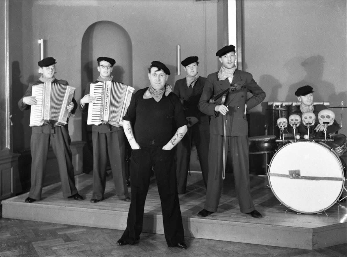 Bert Renées orkester med ordinarie trumslagare främst i utstyrsel som nog ska föreställa en sjöman från sydligare nejder i byxor breda nedtill, "basker", tjusarlock i pannan, scarf och armtatueringar. På bild 2 (med högre upplösning) framgår att det ena dragspelet är av märket Settimio Soprani, vilket är ett av Italiens äldsta varumärken. År 1863 startade Paolo Soprani företaget Soprani tillsammans med sina bröder. Han byggde den första tillverkningsanläggningen på deras bondgård i Castelfidardo. Samarbetet blev kortvarigt för varje broder startade istället sitt eget företag. Settimio tillverkade sina dragspel 1872-1945.
(Se även bildnr GB2_4019-4020)