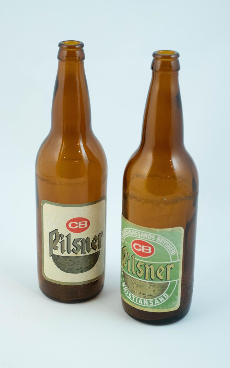 Brune glassflaskre med grønn papiretikett med hvit og lysebrun skrift. På den ene flasken er etiketten falmet hvit.