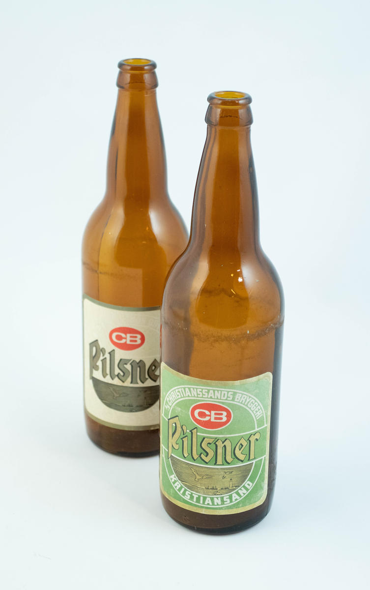 Brune glassflaskre med grønn papiretikett med hvit og lysebrun skrift. På den ene flasken er etiketten falmet hvit.