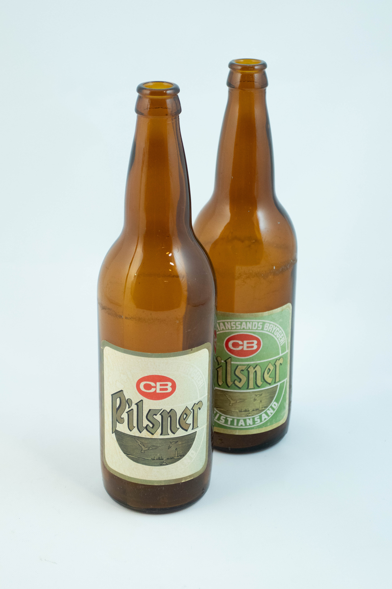 Brune glassflaskre med grønn papiretikett med hvit og lysebrun skrift. På den ene flasken er etiketten falmet hvit.
