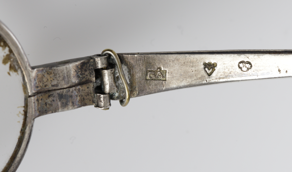 Ett par runda glasögon med skalmar av silver, 
Släta, ledade skalmar (höger ytterled saknas).
Förvaras i hårt, brunt läderetui. 

Inskrivet i huvudkatalogen 1944.
