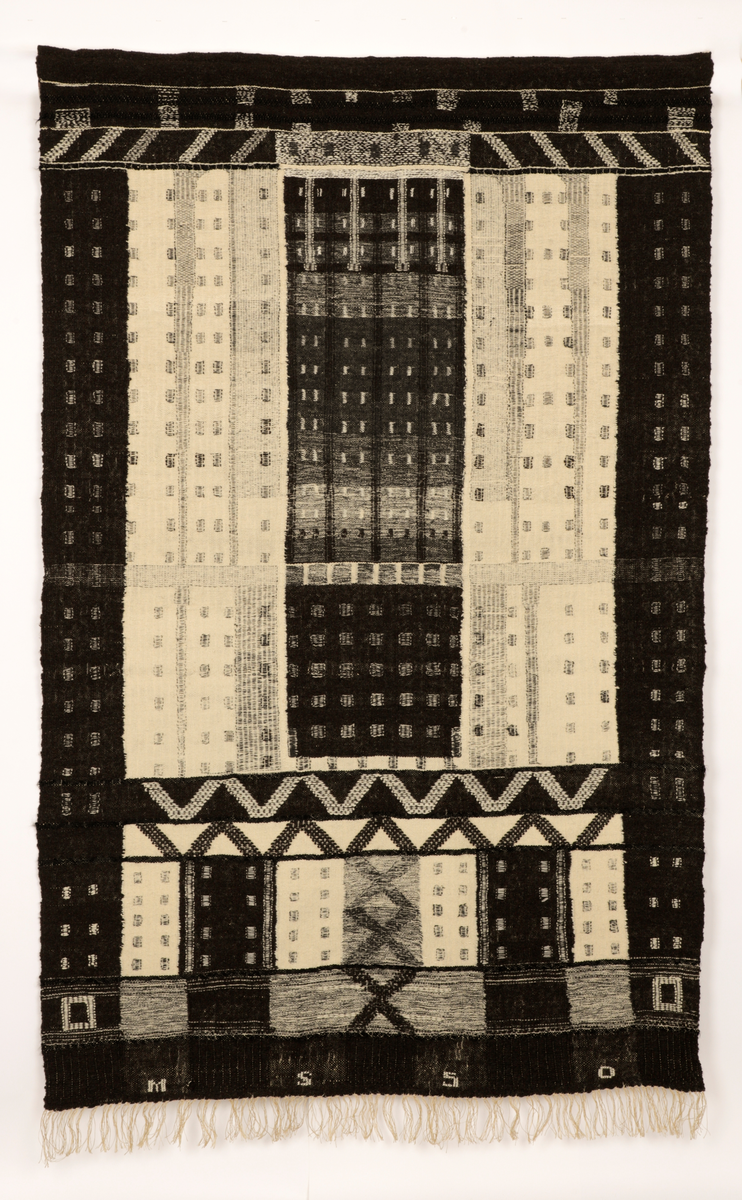 Veggteppe vevd i svart og hvit ull, renning av lin. Fargene fremtrer som nyanser i grått, hvitt og svart. Motivet er inspirert av Manhattans skyskrapere med fremtredende vertikallinjer mønstret av bygningenes vindusrekker. Den nedre del er horisontalbetont med Brooklyn Bridge som inspirerende motiv, tildels med sikksakk-linjer. Frynser nederst.