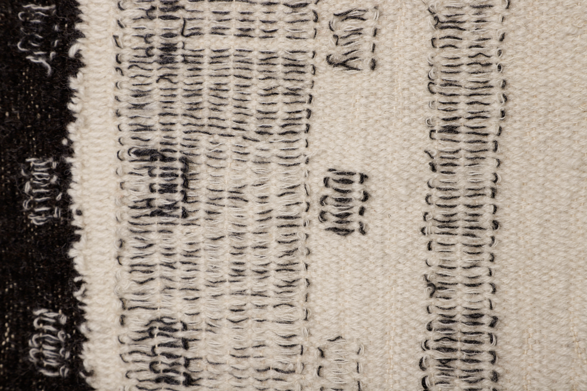 Veggteppe vevd i svart og hvit ull, renning av lin. Fargene fremtrer som nyanser i grått, hvitt og svart. Motivet er inspirert av Manhattans skyskrapere med fremtredende vertikallinjer mønstret av bygningenes vindusrekker. Den nedre del er horisontalbetont med Brooklyn Bridge som inspirerende motiv, tildels med sikksakk-linjer. Frynser nederst.