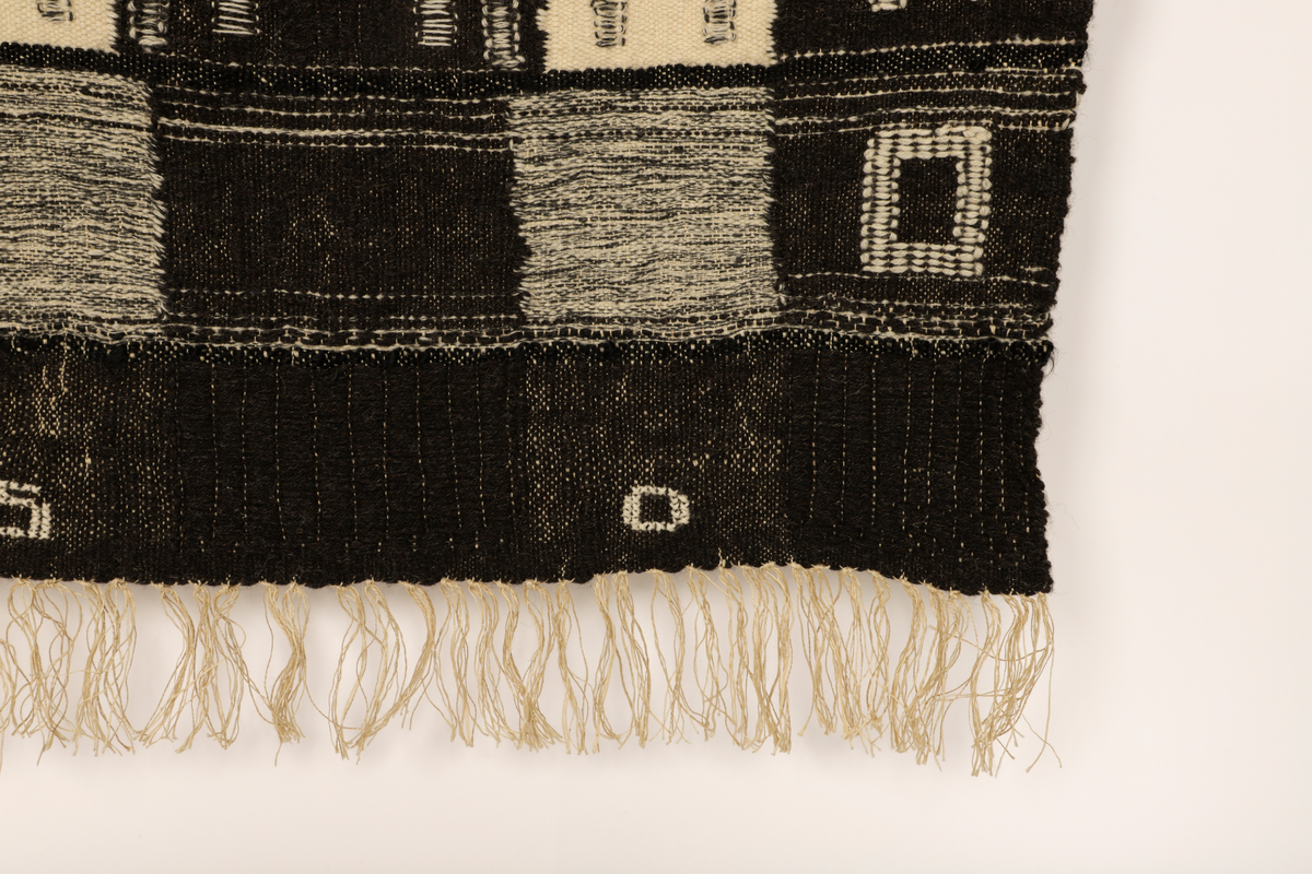 Veggteppe vevd i svart og hvit ull, renning av lin. Fargene fremtrer som nyanser i grått, hvitt og svart. Motivet er inspirert av Manhattans skyskrapere med fremtredende vertikallinjer mønstret av bygningenes vindusrekker. Den nedre del er horisontalbetont med Brooklyn Bridge som inspirerende motiv, tildels med sikksakk-linjer. Frynser nederst.