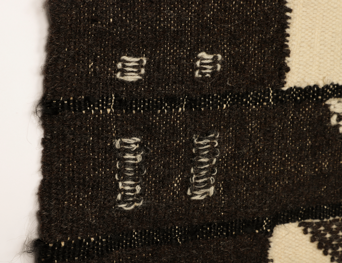 Veggteppe vevd i svart og hvit ull, renning av lin. Fargene fremtrer som nyanser i grått, hvitt og svart. Motivet er inspirert av Manhattans skyskrapere med fremtredende vertikallinjer mønstret av bygningenes vindusrekker. Den nedre del er horisontalbetont med Brooklyn Bridge som inspirerende motiv, tildels med sikksakk-linjer. Frynser nederst.