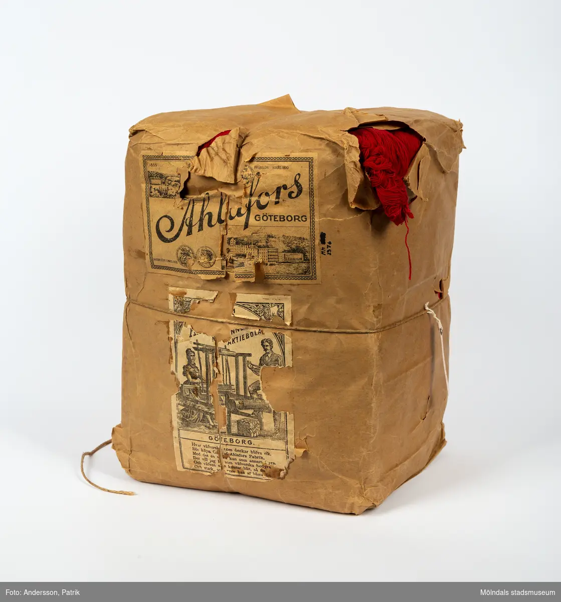 En förpackning med rött bomullsgarn (äkta rödfärg nr 39). Garnmängden (2 kg?) paketerat i brunt omslagspapper, med snöre runt om. Tre olika etiketter från Ahlafors är påklistrade. Pappret är trasigt.Tidigare sakord: garn i förpackning.