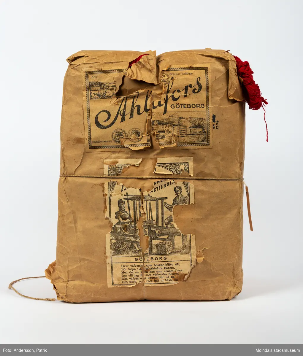 En förpackning med rött bomullsgarn (äkta rödfärg nr 39). Garnmängden (2 kg?) paketerat i brunt omslagspapper, med snöre runt om. Tre olika etiketter från Ahlafors är påklistrade. Pappret är trasigt.Tidigare sakord: garn i förpackning.