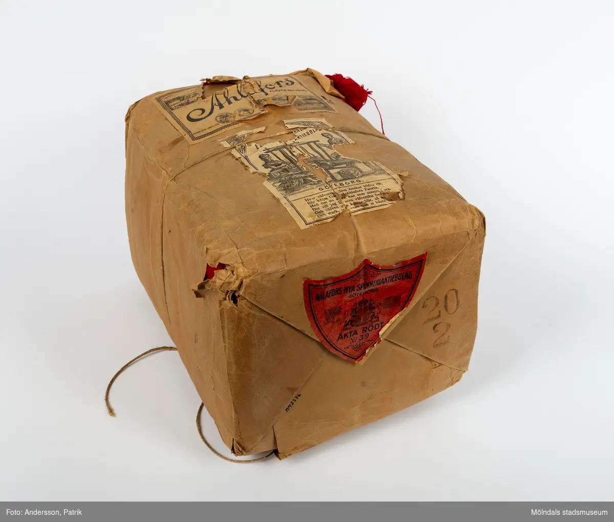 En förpackning med rött bomullsgarn (äkta rödfärg nr 39). Garnmängden (2 kg?) paketerat i brunt omslagspapper, med snöre runt om. Tre olika etiketter från Ahlafors är påklistrade. Pappret är trasigt.Tidigare sakord: garn i förpackning.
