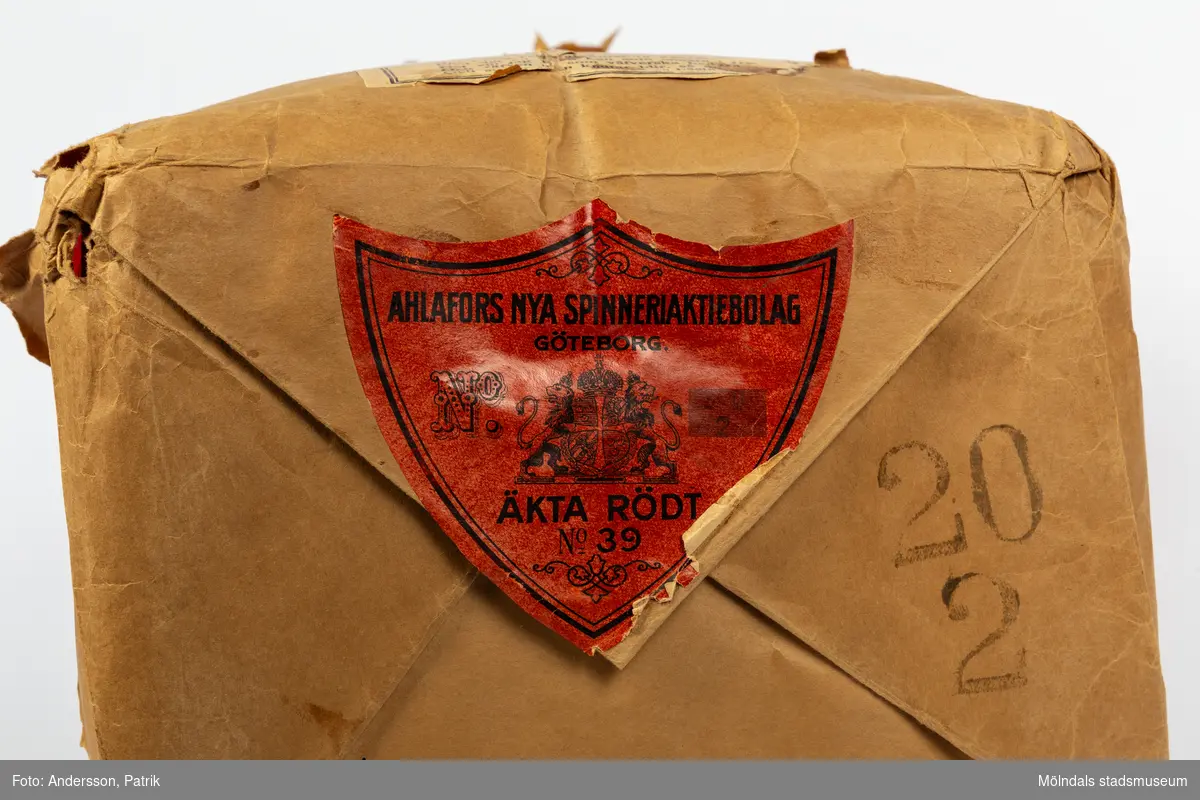 En förpackning med rött bomullsgarn (äkta rödfärg nr 39). Garnmängden (2 kg?) paketerat i brunt omslagspapper, med snöre runt om. Tre olika etiketter från Ahlafors är påklistrade. Pappret är trasigt.Tidigare sakord: garn i förpackning.