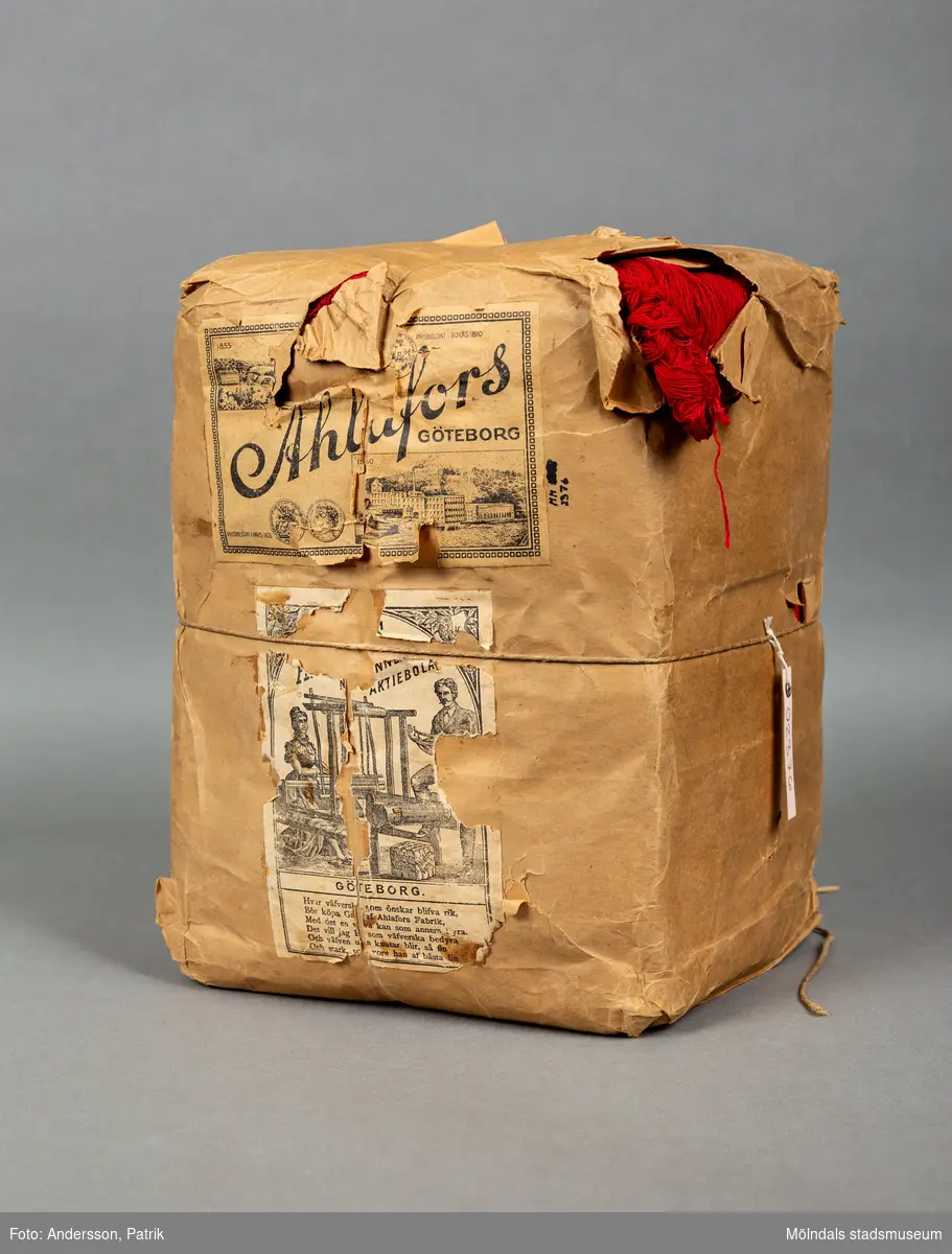 En förpackning med rött bomullsgarn (äkta rödfärg nr 39). Garnmängden (2 kg?) paketerat i brunt omslagspapper, med snöre runt om. Tre olika etiketter från Ahlafors är påklistrade. Pappret är trasigt.Tidigare sakord: garn i förpackning.