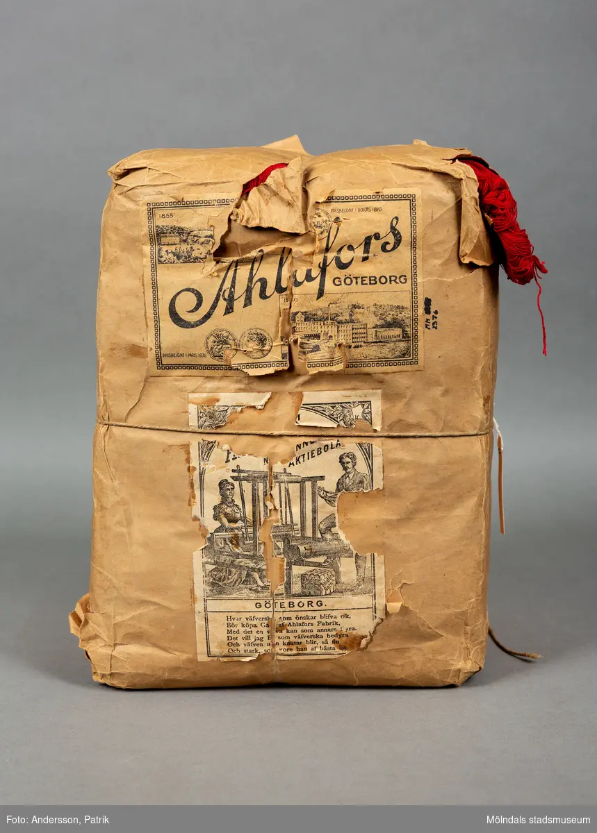 En förpackning med rött bomullsgarn (äkta rödfärg nr 39). Garnmängden (2 kg?) paketerat i brunt omslagspapper, med snöre runt om. Tre olika etiketter från Ahlafors är påklistrade. Pappret är trasigt.Tidigare sakord: garn i förpackning.