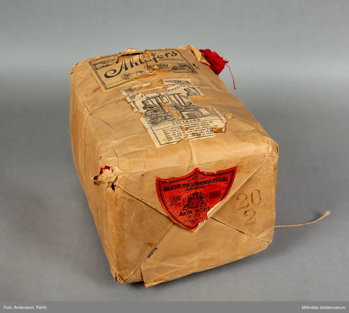 En förpackning med rött bomullsgarn (äkta rödfärg nr 39). Garnmängden (2 kg?) paketerat i brunt omslagspapper, med snöre runt om. Tre olika etiketter från Ahlafors är påklistrade. Pappret är trasigt.Tidigare sakord: garn i förpackning.