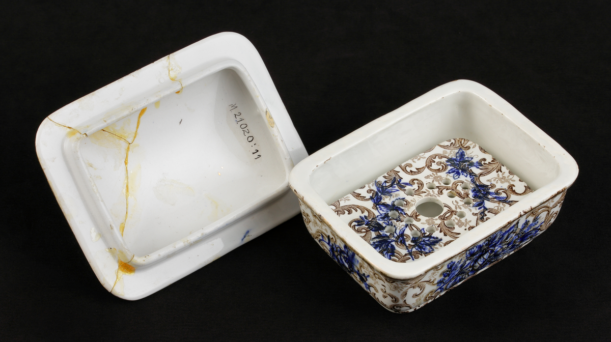Tvålkopp, med lock och bottensil. 
Dekor: akantus, ljusbruna och prickiga slingor på vit botten. 
Djupblå blommor och bladbuketter på in- och utsida. 

Inskrivet i huvudkatalogen 1968.
