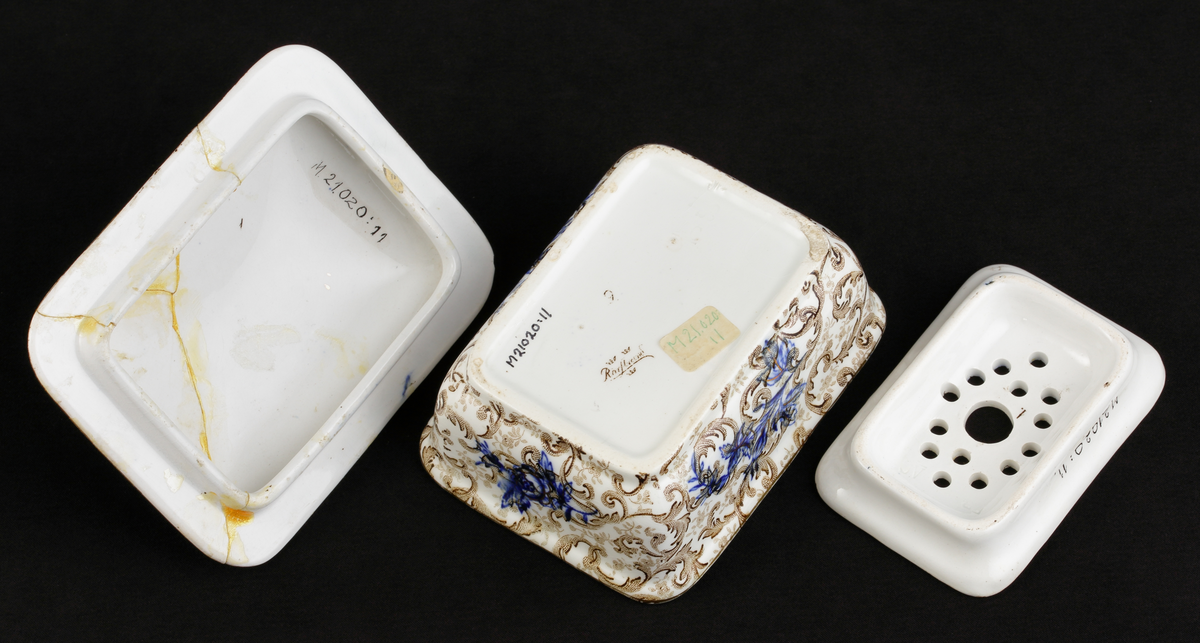 Tvålkopp, med lock och bottensil. 
Dekor: akantus, ljusbruna och prickiga slingor på vit botten. 
Djupblå blommor och bladbuketter på in- och utsida. 

Inskrivet i huvudkatalogen 1968.
