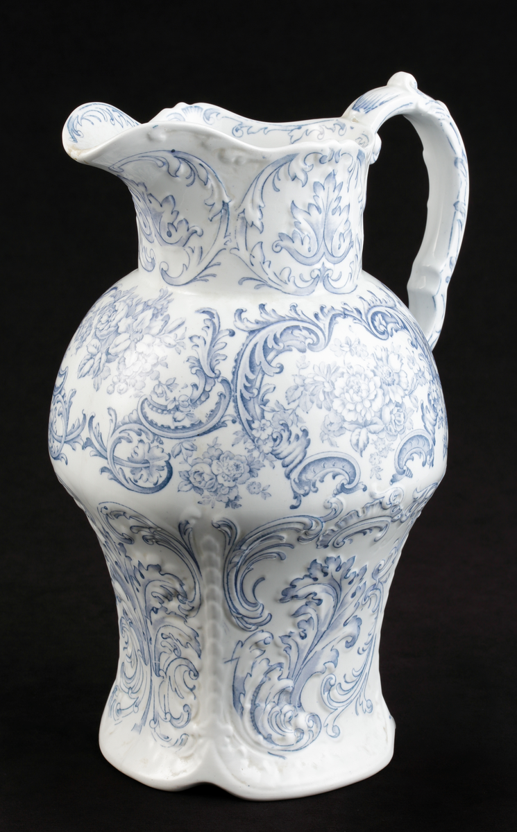 En handkanna av vitt flintporslin. Balustermodell med S-format handtag.
Dekor av blommor och akantusblad med blå kanter, i relief.
Ingår i tvättservis.
