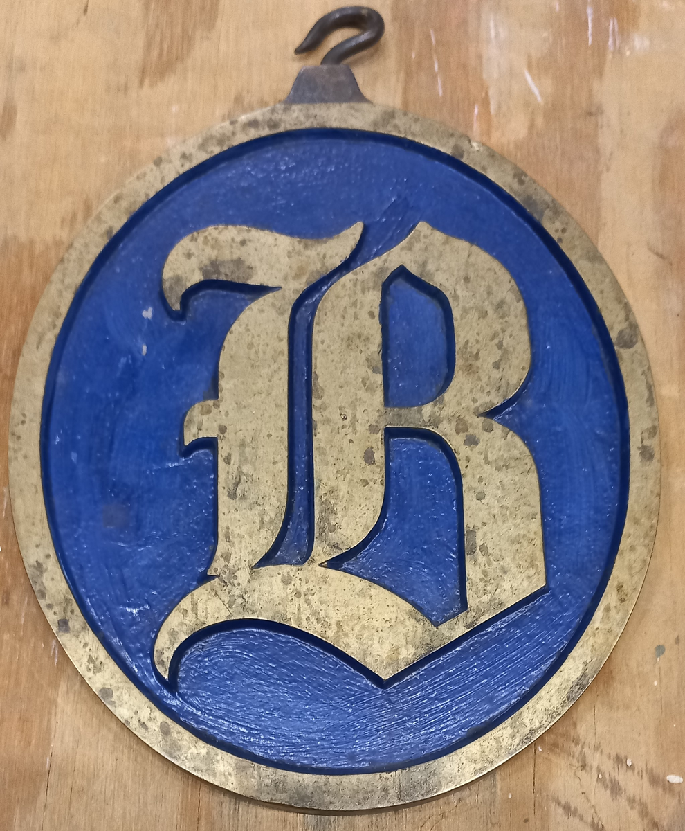 Vaktbricka med upphängningshake, vridbar. B å ena och S å andra sidan.
Blå botten, i övrigt blank. Tillhört  3 kl. pb. Folke.Föremålets form: oval