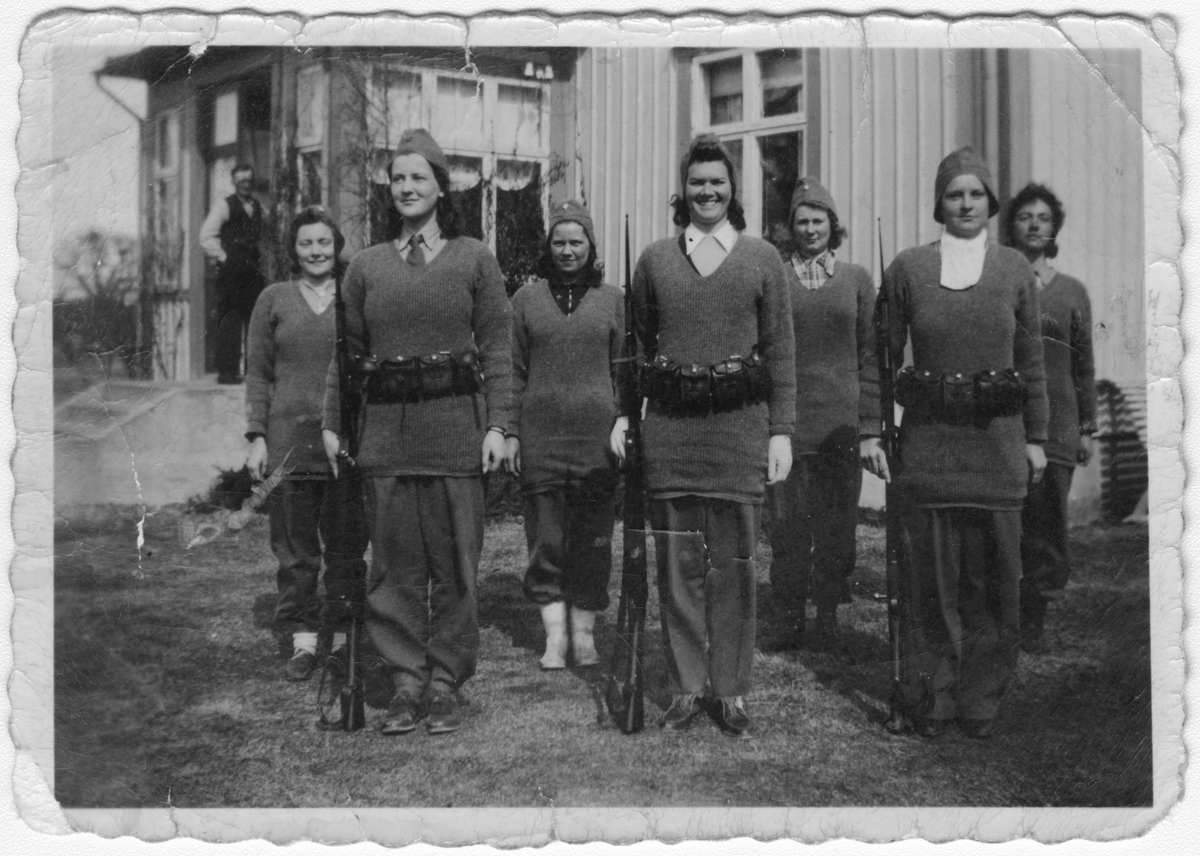 Gruppfotografi av sju luftbevakningslottor i givakt framför hus.
Under luftbevakning på Lurö, Värmland, 1942.