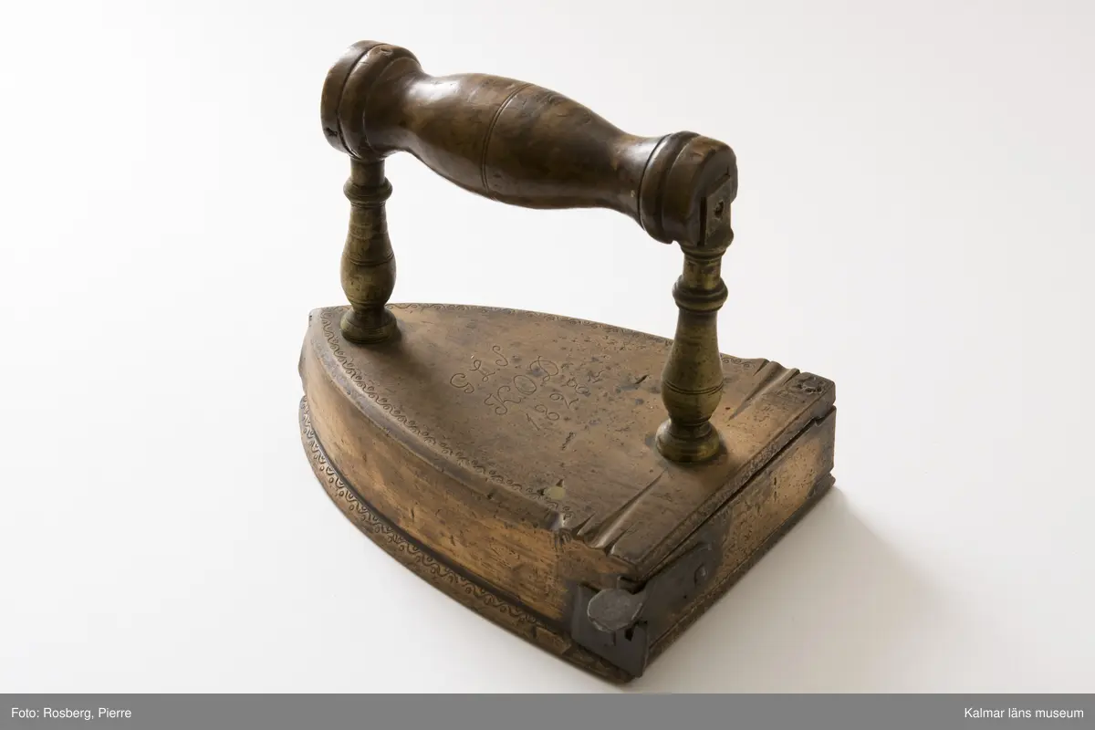 KLM 8512. Strykjärn, lodstrykjärn. Tillverkat av malm, järn och trä. Handtag av trä. På översidan graverat: G.L.S K.O.D. 1828.