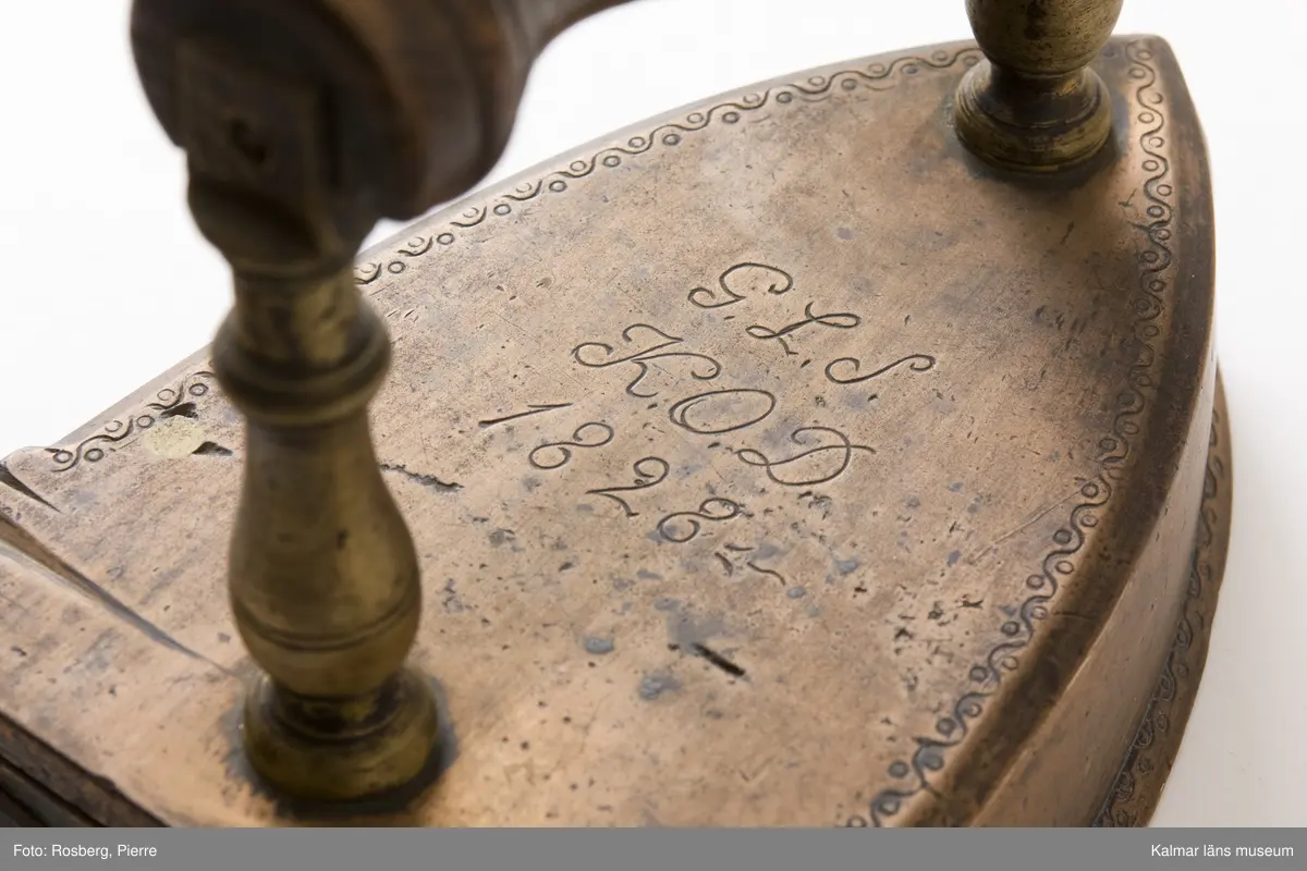 KLM 8512. Strykjärn, lodstrykjärn. Tillverkat av malm, järn och trä. Handtag av trä. På översidan graverat: G.L.S K.O.D. 1828.