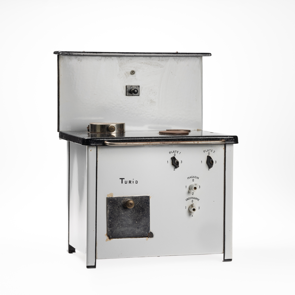 Miniatyrutgave av magasinkomfyr fra KPS. Komfyren har 2 plater, samt ett magasin og stekovnsfunksjon med undervarme. 

Denne komfyren ble spesiallaget  på fritiden av en arbeider ved KPS. Den ble laget til datteren i huset der han hadde husvære (Turid). Han skal også ha laget en til direktørens datter. Borgarsyssel har en maken miniatyrkomfyr som er stemplet KPS - se BrM.11021.