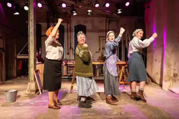 fire kvinner med ullklær og skjørt. De løfter hendene 