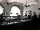 Kunder och personal i kassahallen på Handelsbanken i Oskarshamn 1927. En mycket typisk bild på arbetet i en bank på pennans tid.