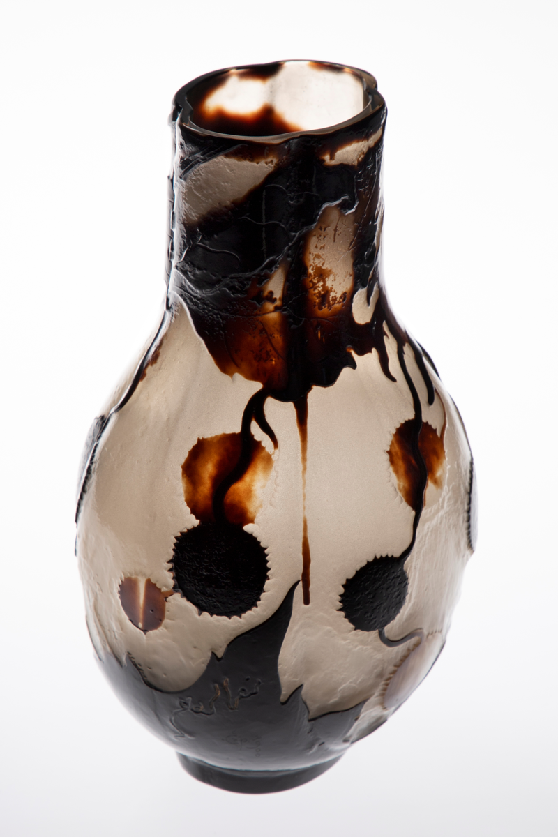 Glassvase med vid hals. Oval utforming med konvekse sider på en sirkulær fot. Overflaten består av en nesten opak gråhvit glassmasse, som er dekorert med blomster og blader fra platantreet i silhuett. Dekorfargen er gradert fra lysebrun til nærmest sort. Signert ”Gallé – Ex. 1900”.