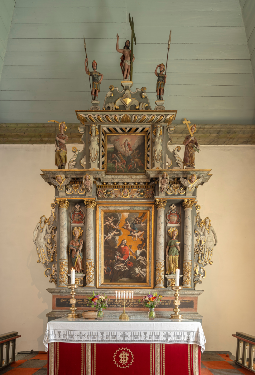 Altertavla og alteret i Tjølling kirke i Vestfold. I Jan W. Krohn-Holms Tjølling bygdebok (bind 1, 1974) beskrives altertavla i soknekirka slik:

«… I 1600-årene kommer også altertavlen til. Den har renessansens søyler og rammeverk, men de har fått en rik utsmykning i bladverk, ornamenter og figurer. Tavlen er blitt til i overgangstiden mellem renessanse og barokk. De har to avdelinger. I den nedre er et maleri av Jesus i Getsemane plassert i midtpartiet, men maleriet er trolig yngre enn selve altertavlen. Mellom søyler står utskårne symbolske figurer, Fortitudo, motets symbolskikkelse, aom holder en del av en søyle, og Prudentia, som symboliserer klokskapen. Hennes attributt er ormen. Utenfor dem igjen, som vanger på tavlen, står engleskikkelser.
Den øvre avdeling har Jesu oppstanselse som billedmotiv i midtpartiet, flankert av to karyatider, mennesker uten armer og underkropp, som har erstattet søylemotivet.
De to symbolske skikkelser på bildene på sidene er Spes, håpet, som bærer et anker, Fides med kors og bok, symbolet på troen.
Helt på toppen av tavlen står Kristus velsignende ved korset, flankert av to romerske soldater.
En innskrift på foten av altertavlen lyder: «Denne Altartaffle haffuer Herre Erich Jenssøn Bugge, Sogne prest til Tiøling Kirche, men sin oc sine Hustruers, S. Randi Iffuersdotters og Randi Pedersdotters Bekostning Gud til Ære oc denne Kirche til beprydelse ladet opreise og forferdige, dog icke os, Herre, men dit Naffn vere æret Ævindelig, 23 Oct. Anno 1634.»
Denne innskriften ble oppdaget i 1930, under restaurering av tavlen. Over innskriften var nemlig lagt et lerretstrekk, med denne tekst: «Rigets Admiral Ove Gjedde Haver gived denne Altar Tafle 1632. Den Høibaarne Comtesse Juliana Sophia af Danneskiold Lauerviig haver ladet den Ziire 1767. J. P. Lindgaard.»
Hvilken av disse to innskriftene som er riktig, eller om de begge er feilaktige, kan vi ikke si med sikkerhet. Et indisium på Ove Gjeddes befatning med tavlen er at han og hans hustrus (Dorothea Urne) våpenskjold er malt på tavlen over symbolskikkelsene, Prudentia og Fortitudio, Men da må det bli avgjørende å finne ut om våpnene er malt i 1632 eller 1767.
I en bok om familen Bygge, som kom ut i 1891, heter det om sogneprest Erik Bugge at «han lod Altertavlen forferdige og opsætte på Admiral Ove Gjeddes Bekostning 1632». Kanskje er vi her inne på det riktige, et samarbeide mellom prest og lensherre.»

På alterets ytterkanter står to høye, tunge messinglysestaker, som også skal ha vært gaver fra Ove Gjedde.