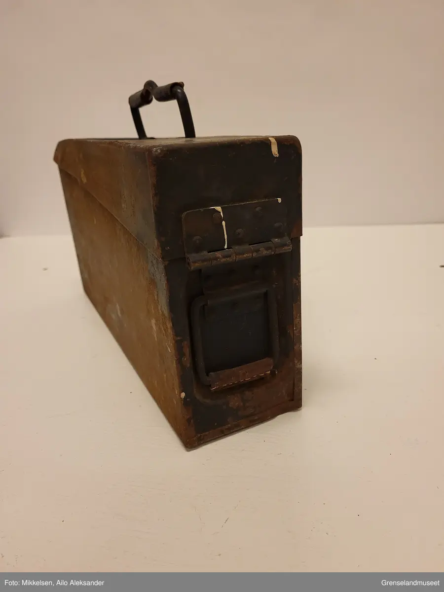 Gjenstanden er en svart malt ammunisjonskasse av jern metall som har vært brukt av tyske mitraljøsetropper under andre verdenskrig. Ammunisjonskassen har tre håndtak med sitt originale lærreimer til å dekke metallet. På venstre side over håndtak er åpne/lukke mekanismen til ammunisjonsboksen, den er i god stand og fungerer uten problemer. Innsiden av gjenstanden er blank og uten skader, bortsett fra litt rødt jern sverting. Bortsett fra riper, avskalling fra den svarte lakken og litt rød jern sverting, er gjenstanden i god stand  