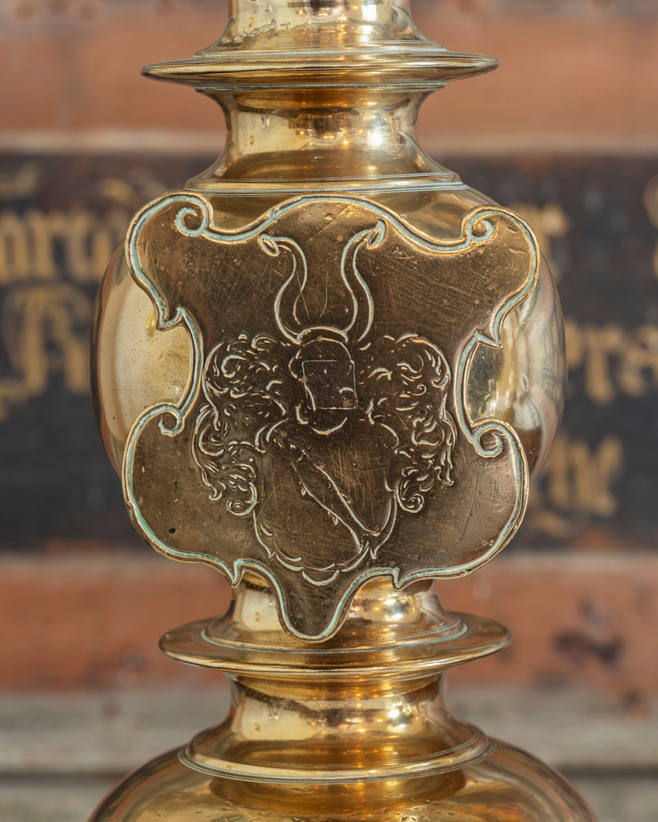 Skjoldformet messingplate med embetsmannen og offiseren Ove Gjeddes våpenskjold. Motivet er ei skråstilt gjedde i skjoldet og to vesselhorn som hjelmtegn. Det er inngravert en av to høye, tunge lysestaker som står på ytterkantene av alteret i Tjølling kirke i Vestfold. Stakene skal ha vært gaver fra nevnte Ove Gjedde, som i en periode bodde i dette prestegjeldet. Litt biografisk informasjon om ham finnes under fanen «Opplysninger».
